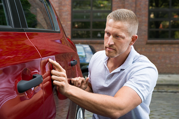 Image of man looking at damage on a red car.